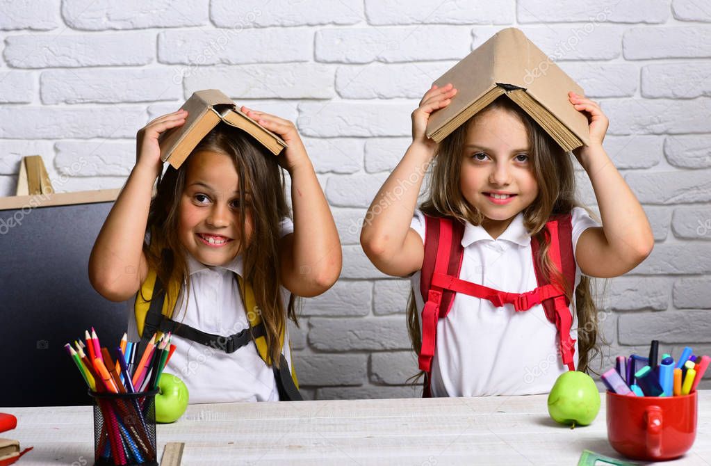 Cheerful smiling little girls with books on head. Looking at camera. School concept. Back to School.