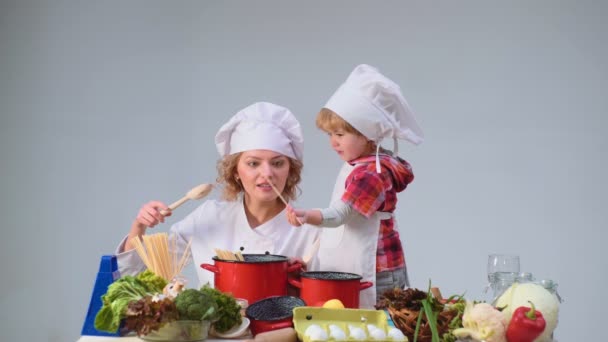 Ładny mały chłopiec i jego piękna matka uśmiechający się podczas gotowania w kuchni. Młode rodziny gotowanie jedzenie w kuchni. Młoda matka i syn, wspólne gotowanie posiłków. — Wideo stockowe