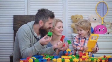 Genç aile inşaat plastik blokları ile oyun oynamak. Aile Oyunları kavramı. Anne ve çocuk mutlu yüzler ile kırmızı tuğla tutun. Baba, anne ve oğlu ışık ahşap arka plan üzerinde oyun odası.