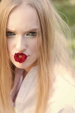Bayan gün 8 Mart, Bahar kavramı. Kadın ağzına kırmızı çiçek ile 8 Mart. Uzun sarı saçlı, doğa üzerinde saç moda modeli. Glamour kızla güzellik bak, makyaj