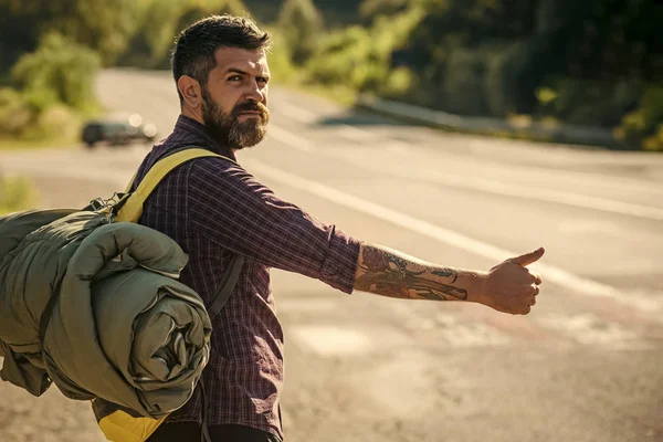 Человек с рюкзаком автостопом на дороге — стоковое фото