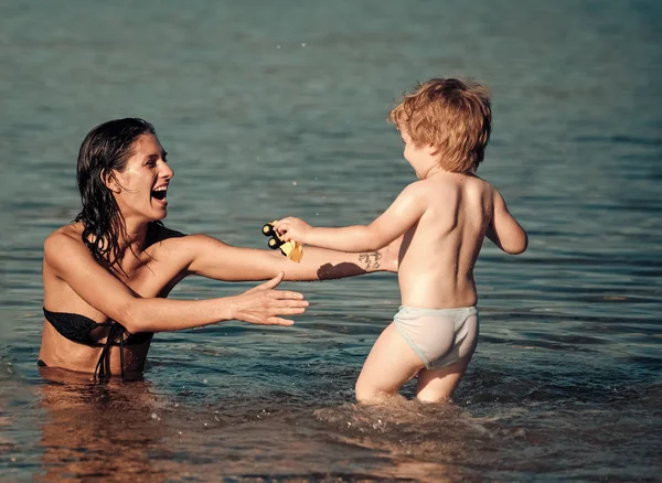 Милый мальчик играет с мамой в море, океане. Мама и ребенок с улыбкой проводят время вместе в море в солнечный день. Концепция материнства. Мать плавает в море и смотрит на ребенка — стоковое фото