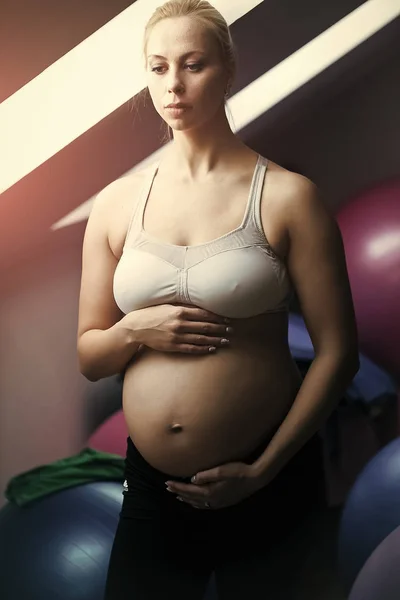 Woman touching pregnant belly with hands in gym with balls — Stock Photo, Image