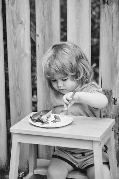 Menino pequeno comer torta perto de cerca de madeira — Fotografia de Stock