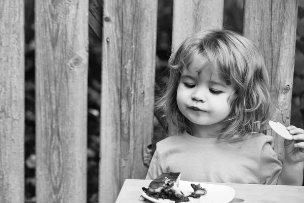 Piccolo ragazzo mangiare torta vicino recinto di legno — Foto Stock