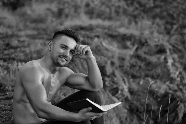 Uomo muscoloso sorridente con libro all'aperto — Foto Stock