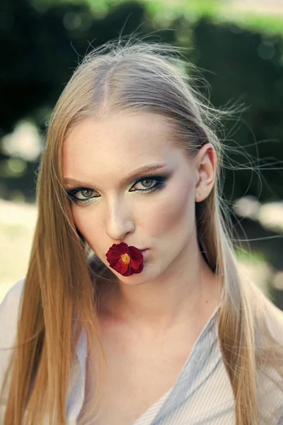 Mujer con flor roja en la boca, 8 de marzo. Modelo de moda con pelo largo y rubio, peinado en la naturaleza. Día de la mujer, 8 de marzo, concepto de primavera. Chica de belleza con aspecto glamuroso, maquillaje . — Foto de Stock