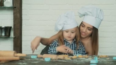 Mutlu aile birlikte fırın hazırlıyor. Anne ve kız çocuk kurabiye pişiriyor ve mutfakta eğleniyorlar. Ev yapımı yemek ve küçük bir yardımcı..