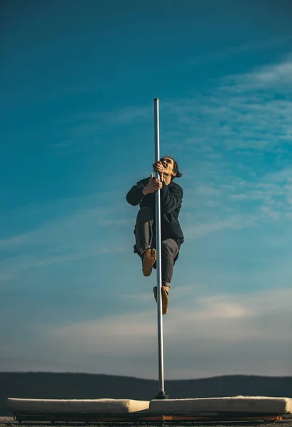 Pole dance sport. pole dance training of young man dancer on blue sky background.