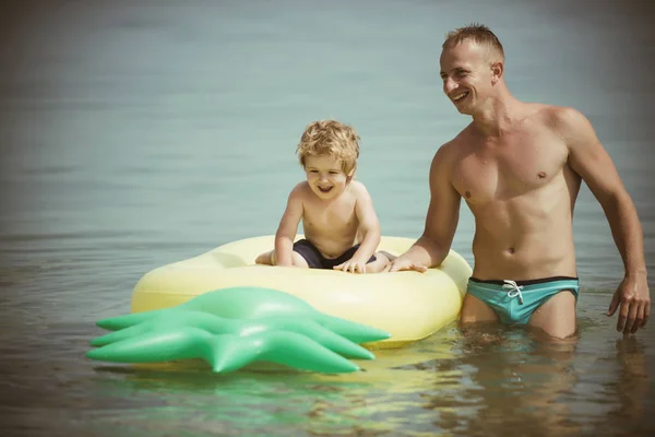 Malediven oder Mami Strand Aktivität Freude. Vater und Sohn schwimmen am Vatertag im Wasser. Ananas aufblasbare oder Luftmatratze. glückliche Familie am karibischen Meer. Sommerurlaub und Reise ans Meer, Jahrgang. — Stockfoto