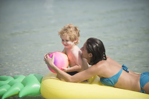 子供を持つ母は、夏に、水遊びで空気マットレスの上ボールを再生します。. — ストック写真