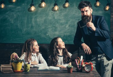 Öğretmen ve kız öğrencilerin sınıfta, kara tahta arka plan. Öğretmen dikkat ile dinleme meraklı çocuk. Sakallı resmi kıyafetli kız öğrenciler öğretir. İlköğretim Okulu kavramı.