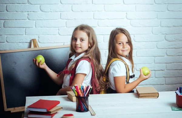 Las niñas comen manzana en la hora del almuerzo. Niños de la escuela feliz en la lección en septiembre 1. Amistad de las hermanas pequeñas en el aula en el día del conocimiento. De vuelta a la escuela y a la educación en casa. Tiempo escolar de las niñas — Foto de Stock