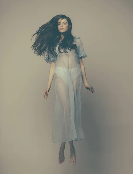 Teenage girl in blue gown jumping isolated on dimmed beige background. Young nymph in light silk dress flying in air. Lightness and levitation, airiness concept — Stock Photo, Image