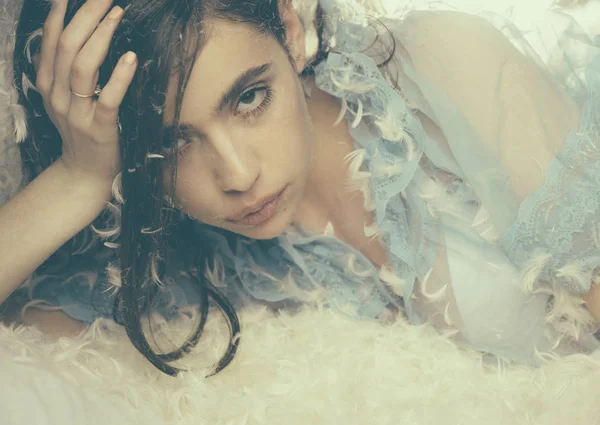 Mujer con el pelo largo en pijama tierno relajante. Chica en la cara tranquila yacía en la cama cubierta de plumas y pelusa. Concepto suave y suave. Señora en camisón azul transparente yacía en la cama, de cerca . — Foto de Stock