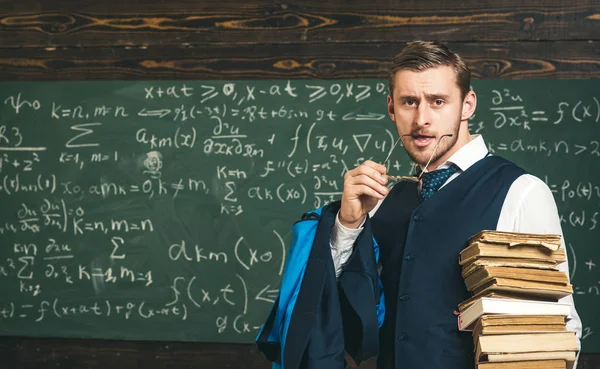 Ritratto di giovane uomo sicuro di sé con mucchio di libri. Studente biondo con in mano un auricolare dei suoi occhiali in bocca — Foto Stock