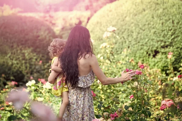 Woman hold child girl at blossoming roses on idyllic day