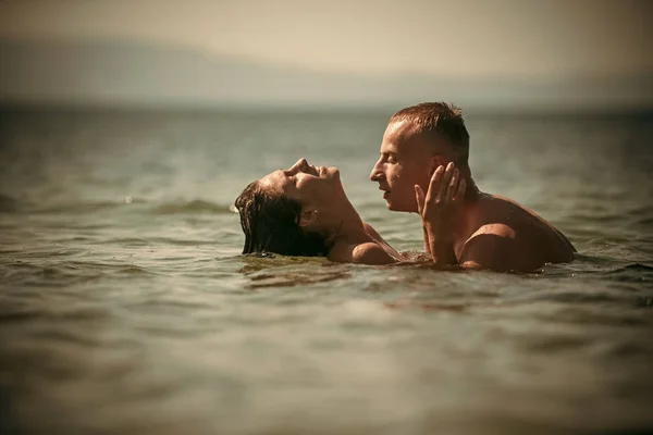 Um casal cheio de abraços de desejo no mar. Casal no amor abraços e beijos na água do oceano. Menina nua com macho faz amor. Amor e conceito romântico. Morena com amante apaixonado bonito . — Fotografia de Stock