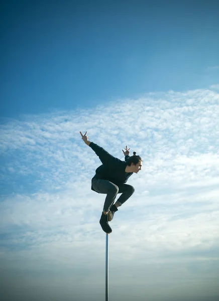 Ejercicio de bailarín hombre fuerte en poste. Joven bailando sobre pilón. Hombre macho sexy volar sobre el fondo del cielo azul. Pole dance sport. El atlético hace elementos acrobáticos en pilón. Mañana hacer ejercicio . — Foto de Stock