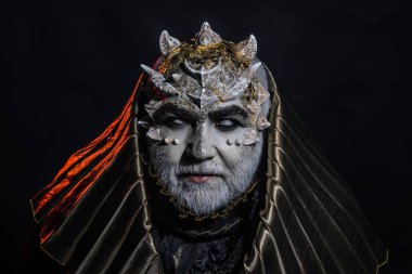 Beyaz sakallı komuta sizde canavar gibi giyinmiş. Fantezi kavramı. Adam dikenler veya siğiller ile yüz pırıltılar ile kaplı. Siyah zemin üzerine altın kukuleta ile iblis. Uzaylı, iblis, büyücü makyaj.
