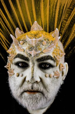 Dikenler veya siğiller, baş yüz pırıltılar ile kaplı, yakın çekim. İblis altın yaka, siyah arka plan ile. Uzaylı, iblis büyücü makyaj. Fantezi kavramı. Sakallı canavar makyaj ile üst düzey adam.