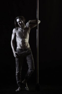 Yorgun dansçı kavramı. Adam çıplak gövde ile parıldayan gümüş boya, koyu arka plan ile kaplı. Adam metalik kutubun yalın. Adam çıplak göğüs, atlet, kutup dans hamle yapmak sporcu ile.