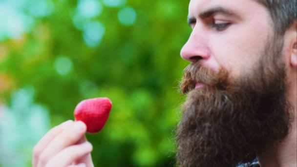 Perto de um jovem a comer um morango. homem comendo um morango como parte de um jogo sexual. Jovem segurando um morango e sorrindo . — Vídeo de Stock