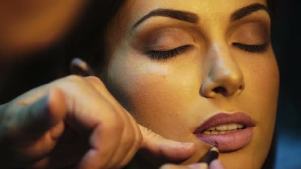 Artista de maquilagem que aplica batom brilhante em lábios de modelos. Maquiagem artista fazendo maquiagem para menina interior . — Vídeo de Stock