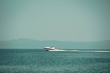 Arka plan üzerinde yüksek sürat teknesi deniz, mavi gökyüzü ve dağlar. Beyaz lüks yatta görünümü şaşırtıcı deniz yüzeyi üzerinde süzülüyor. Güzel mavi deniz gemide sonra beyaz dalgalar. Turizm ve tatil kavramı
