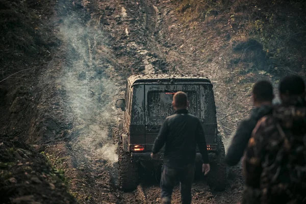 Společnost tří mužů se dívá na suv jednotky s kouřem. — Stock fotografie