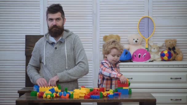 父と息子の笑みを浮かべて、グッズ レンガでカラフルな構造を作成します。お父さんと子供のおもちゃでは、プラスチック製のブロックの構築します。男と少年は一緒に遊ぶ。家族および幼年期の概念. — ストック動画