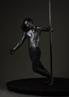 Adam çıplak gövde ile parıldayan gümüş boya, koyu arka plan ile kaplı. Genç seksi gizemli atlet moda vurdu. Maço çıplak göğüs, atlet, sporcu ile metalik direği tut. Moda kavramı