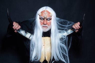 Cadılar Bayramı canavarı gibi giyinmiş yaşlı sakallı bir adam. Kötü vampir adam. Şeytan korku konsepti. Sihir ve masal kavramı. Drakula - Cadılar Bayramı konsepti. Şeytan boynuzları. Yaşlı adam iki kırmızı boynuz tutuyor..