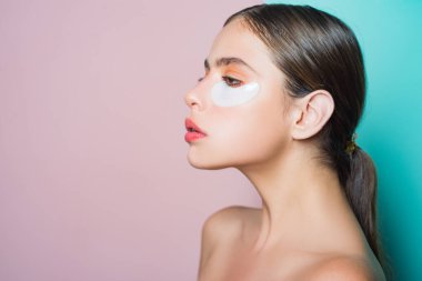 Doğal güzellikte bir kadın cilt bakımı yapar. Göz tedavisiyle. Rüya gibi çekici kız gözlerinin altına kolajen bantları yapıştırıyor. Çıplak omuzlu bir kadın cildine dikkat eder..