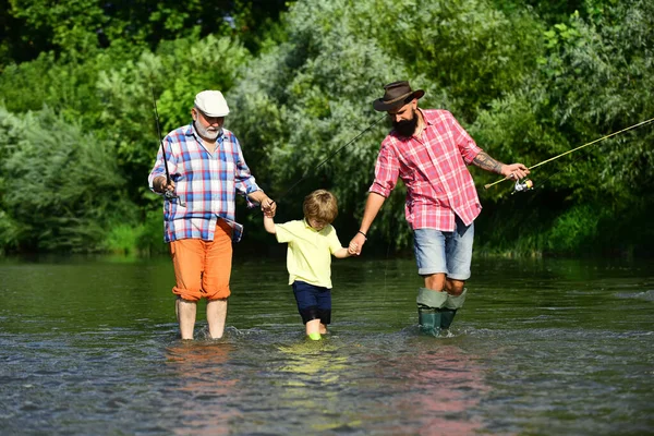 Three generations ages: grandfather, father and young teenager son. Father, son and grandfather relaxing together. Fly fisherman using fly fishing rod in river.