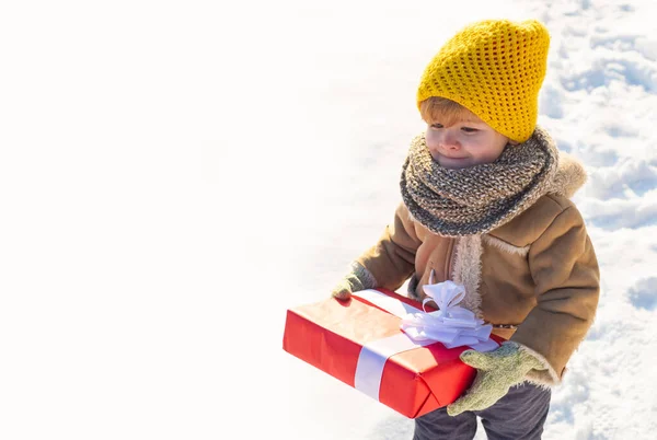 A criança na roupa de inverno mantém o presente de Natal. Criança durante um passeio em um parque de inverno nevado. Bela natureza de inverno. Incrível parque de Inverno. Criança adorável com rosto bonito. Ptoto com espaço de cópia vazio. — Fotografia de Stock