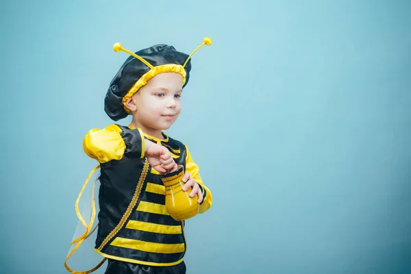 Petit garçon drôle dans un costume d'abeille. Joli garçon habillé en costume de carnaval. Une jolie petite abeille mange du miel. Costume de carnaval. Isolé sur bleu . — Photo