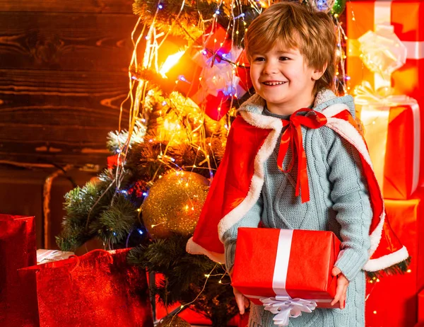 Glad leende pojke som håller sin julklapp. Förvånad unge på nyår dekorerad bakgrund. Familjesemester och människor koncept. Barndoms ögonblick. Julattribut. — Stockfoto