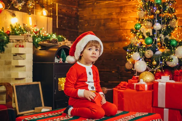 Lindo bebé de santa con regalos de año nuevo en el fondo navideño. Celebrando la Navidad juntos. Niña elfa. Regalos para las vacaciones de invierno en la chimenea. Es un milagro. . — Foto de Stock