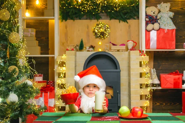 Dia de Acção de Graças e Natal. Feliz Papai Noel - menino bonito criança comer um biscoito e beber um copo de leite em casa interior de Natal . — Fotografia de Stock