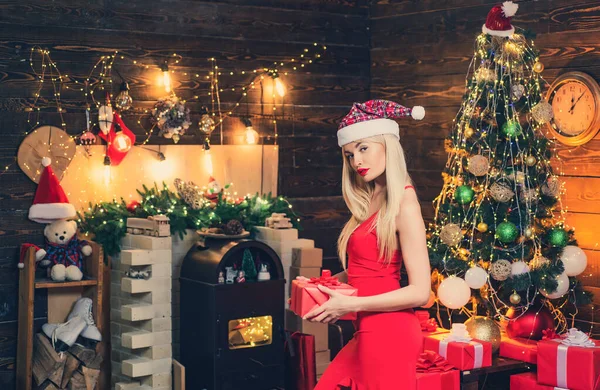 Gelukkige vrouw met kerstcadeau over kerst interieur achtergrond. Vrouw in rode jurk bij de kerstboom. Kleurrijke make-up en retro kapsel voor Kerstmis of Nieuwjaar feest. — Stockfoto