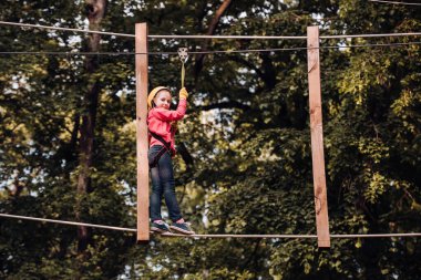 Küçük çocuk macera parkına kask ve güvenlik ekipmanıyla tırmanıyor. Çocuk macerası ve seyahat. Güzel küçük çocuk tırmanıyor ve macera parkında eğleniyor..