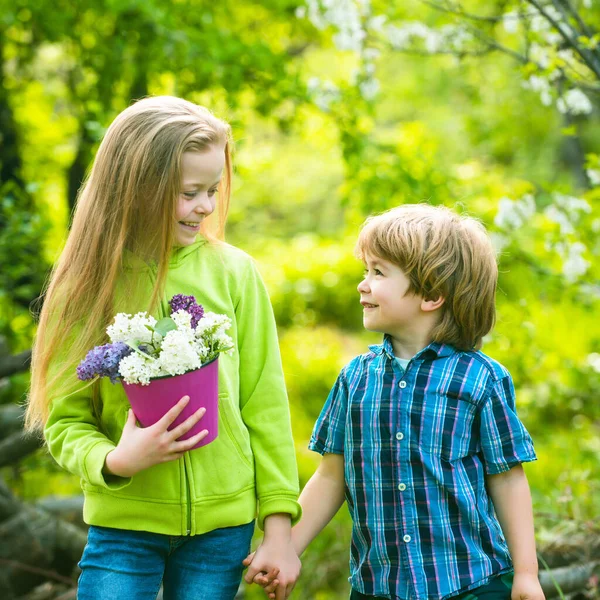 Cheerful smiling boy and girl look at each other and walk outdoor. First love and childhood concept. Little boy and girl holding hands. Children have fun in the spring garden. — Stock Photo, Image