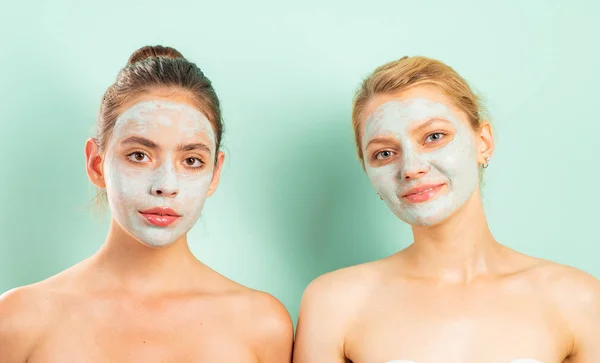 Dvě přírodní krásné kamarádky dívky s hliněnou bahenní maskou na obličeji dělají zdravou péči o pleť. Zdraví a krása. Detail portrét nejlepších přátel izolovaných na světle modrém pozadí. — Stock fotografie