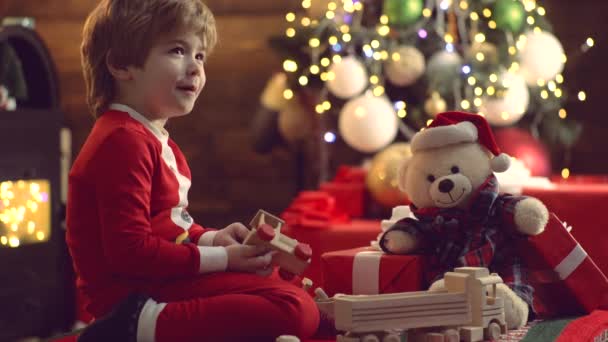 Şirin küçük çocuk Noel ağacını içeride süslüyor. Kışın giyinmiş küçük mutlu çocuk Noel ağacının yanında Noel Baba 'yı düşün. Yeni yıl Noel konsepti. — Stok video
