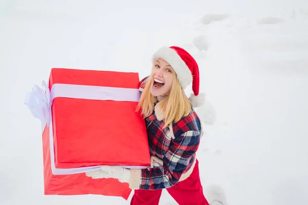 Femmes de service avec grand coffret cadeau. Santa femme tient une grande boîte cadeau avec de l'espace de copie pour votre texte. Joyeux hiver. Femme portant un gros cadeau isolé sur fond d'hiver de neige . — Photo