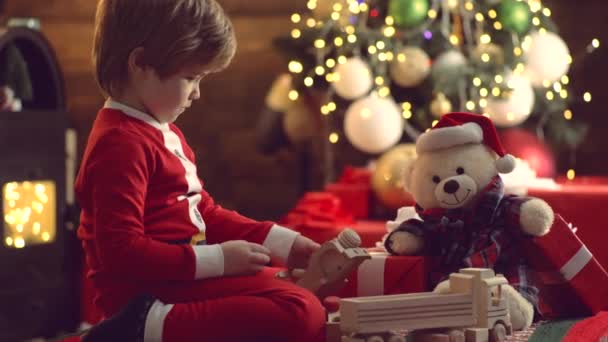 Criança de Natal em chapéu de Santa com presente tem um Natal. Criança bonita perto da árvore de Natal. Crianças - conceito de felicidade. A manhã antes do Natal . — Vídeo de Stock