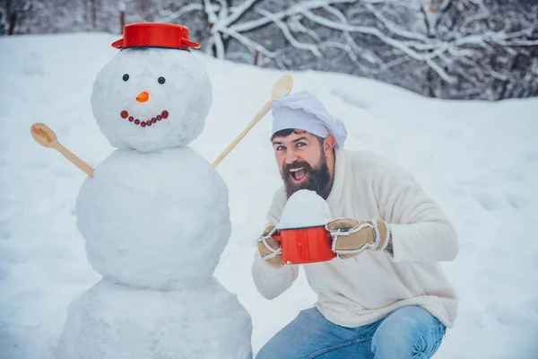 Cuisine de Noël. Drôle de cuisinier de Noël. Joyeux père cuisinier jouant avec un bonhomme de neige lors d'une promenade hivernale enneigée. Père Noël souhaits de cuisine Joyeux Noël. — Photo