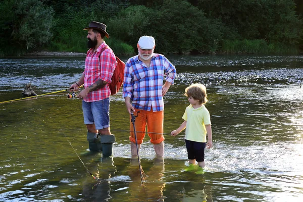 Чоловік з сином і батьком на річковому риболовлі з риболовецькими паличками. Хлопчик з батьком і дідусем літають на риболовлю над річковим тлом . — стокове фото