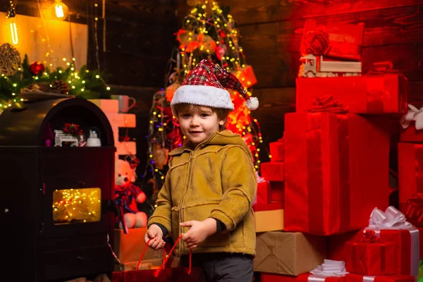 Criança de Natal usando chapéu de Papai Noel no fundo da árvore de Natal. Conceito de férias. Criança com presente de Natal nas mãos . — Fotografia de Stock